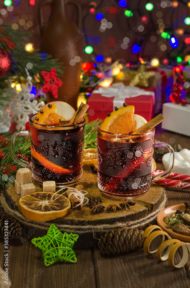 Naklejka premium Mulled wine with orange slice, cinnamon stick on the background of festive garland lights. Dark style