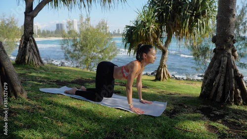 Young Woman In Sportswear Doing Yoga Poses For Back Pain - Cat To Cow Yoga Pose Exercise On Mat - Burleigh Heads Beach In Queensland, Australia. - wide shot photo