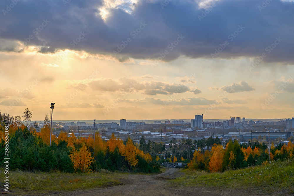 View of the evening autumn forest and the city, top view. View of the city from the mountain and yellowed trees along the road