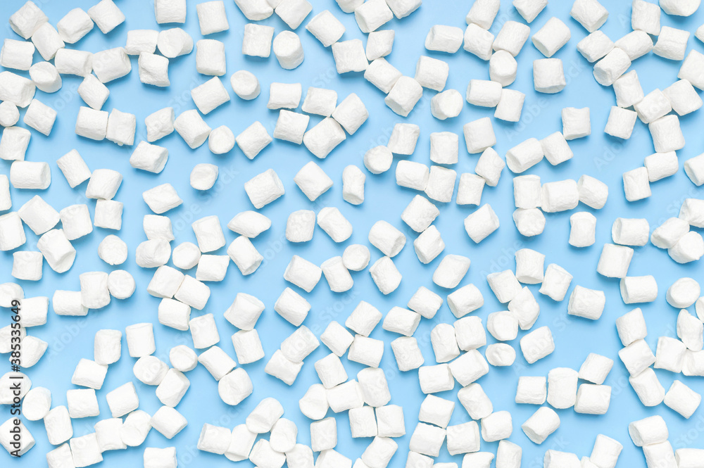 White sweet marshmallows on blue background flat lay top view copy space. Winter or autumn food concept, New Year's or Christmas sweetness, candy, dessert. Marshmellow texture. Minimalistic style