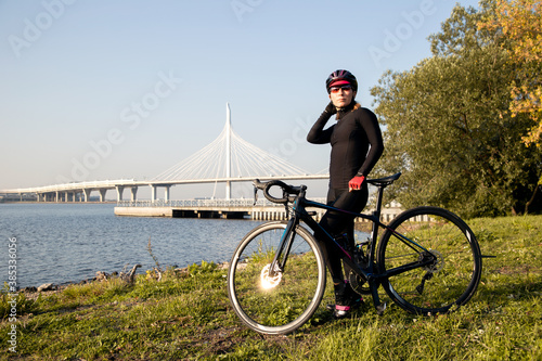 Fototapeta Naklejka Na Ścianę i Meble -  Portrait of a woman cyclist on the shore of the Gulf of Finland against the background of a cable-stayed bridge. Outdoor cycling. Morning workout.