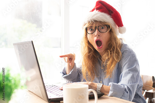 woman in office or home with computer santa claus hat and expression of astonishment or surprise