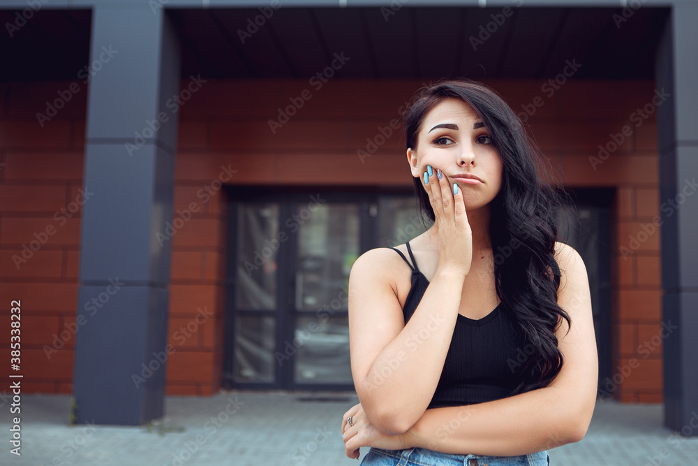Portrait of young woman get bored, looking tired while standing outside, dressed in black singlet and looking away. Image with copy space.
