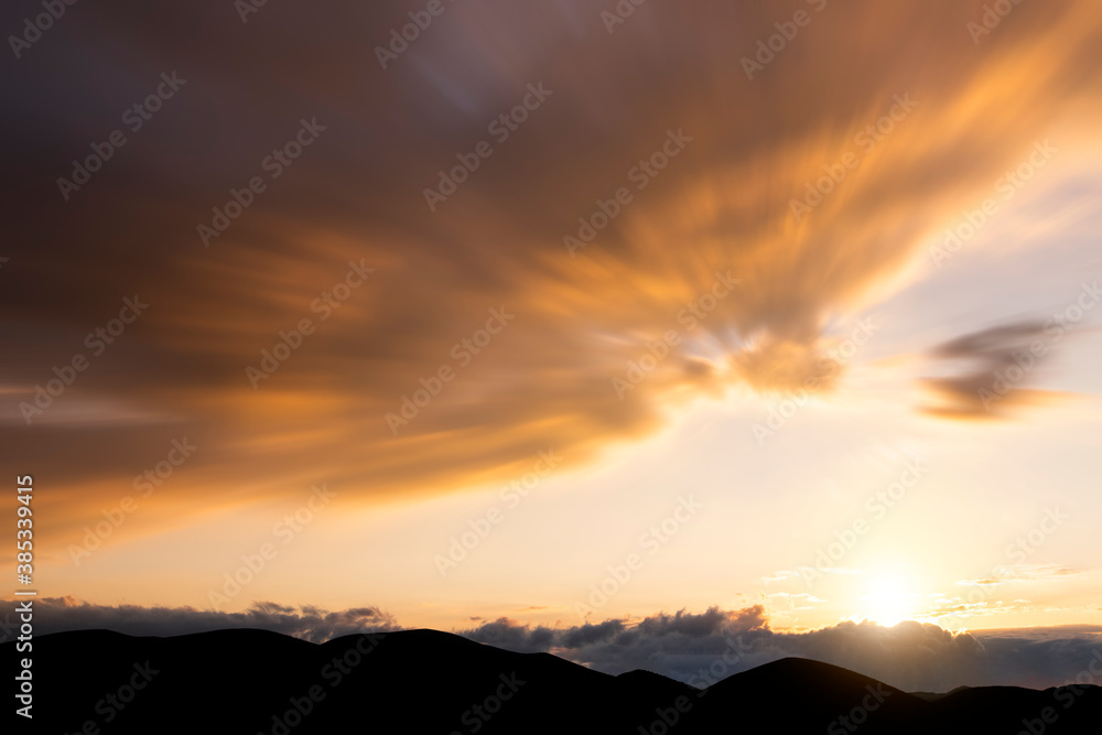 Beautiful long exposure sunset clouds on the bright sky over the mountains.