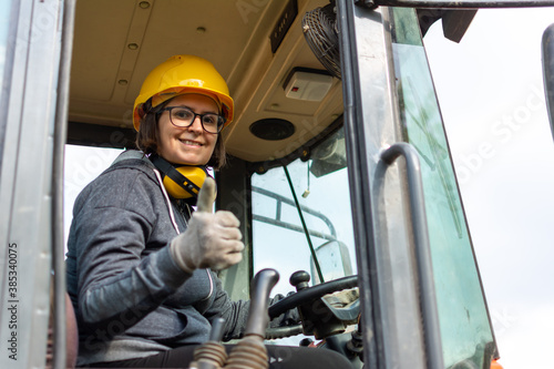cheerful female excavator operator on construction site. Woman construction apprentice learning to drive heavy equipment photo