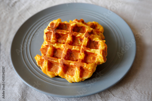 fresh Belgian waffle made from cornmeal, eggs and pumpkin is laid on a grey round plate on a beige tablecloth side view . gluten-free homemade food