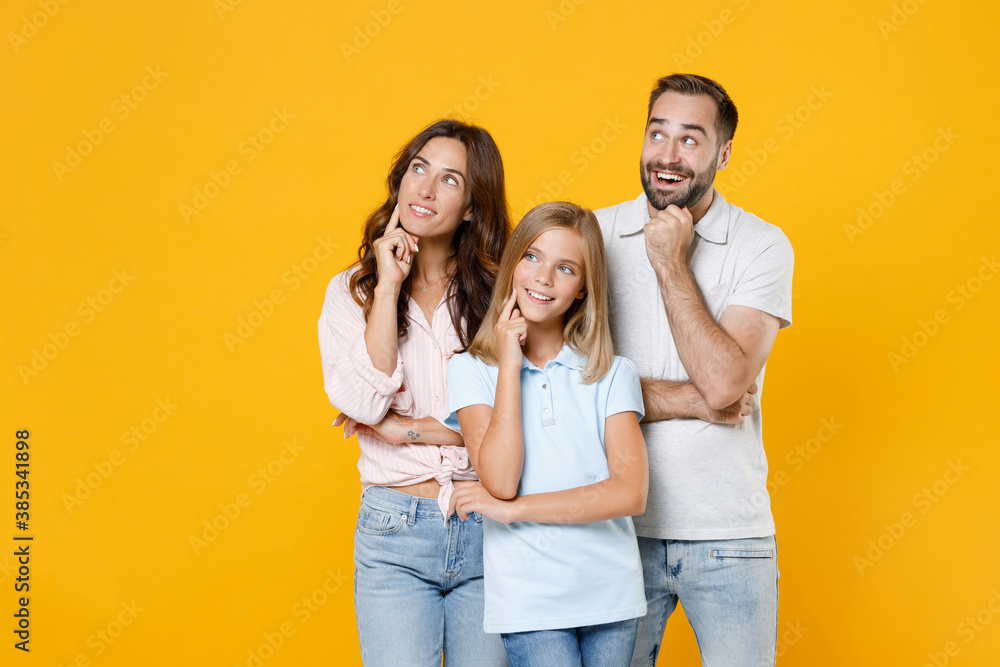 Pensive young parents mom dad with child kid daughter teen girl in basic t-shirts put hand prop up on chin looking aside isolated on yellow background studio portrait. Family day parenthood concept. Pensive young parents mom dad with child kid daughter teen girl in basic t-shirts put hand prop up on chin looking aside isolated on yellow background studio portrait. Family day parenthood concept.