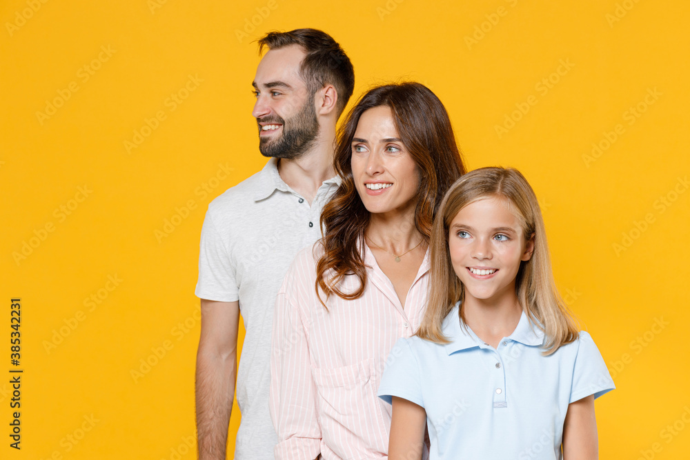 Smiling funny young happy parents mom dad with child kid daughter teen girl in basic t-shirts looking aside isolated on yellow background studio portrait. Family day parenthood childhood concept. Smiling funny young happy parents mom dad with child kid daughter teen girl in basic t-shirts looking aside isolated on yellow background studio portrait. Family day parenthood childhood concept.