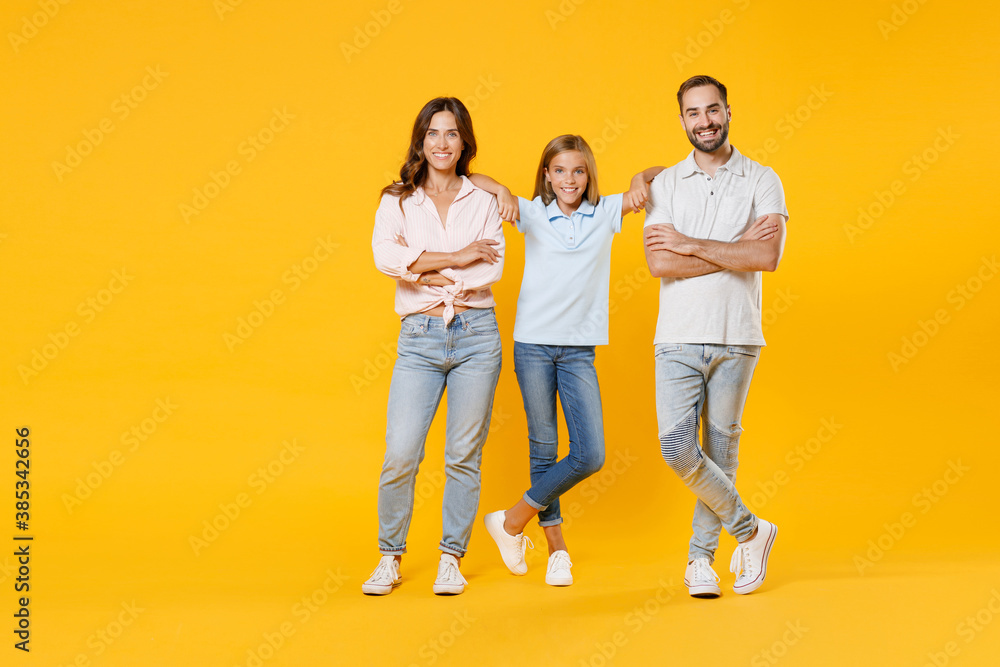Full length portrait smiling young parents mom dad with child kid daughter teen girl in basic t-shirts jumping holding hands crossed isolated on yellow background studio portrait. Family day concept. Full length portrait smiling young parents mom dad with child kid daughter teen girl in basic t-shirts jumping holding hands crossed isolated on yellow background studio portrait. Family day concept.