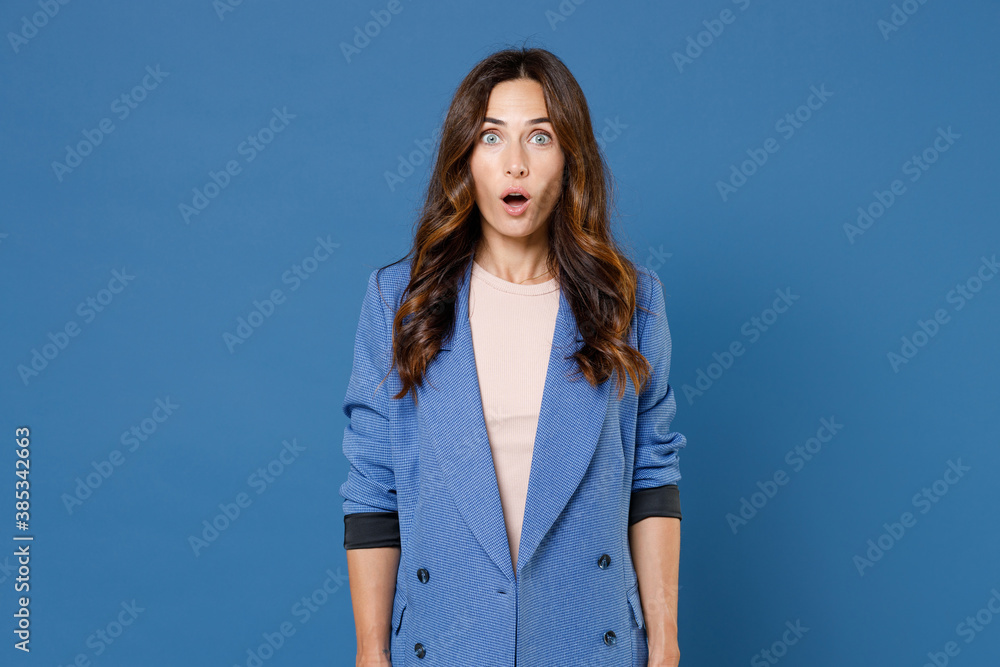Shocked amazed surprised attractive young brunette woman 20s wearing basic jacket standing keeping mouth open saying wow looking camera isolated on bright blue colour background, studio portrait. Shocked amazed surprised attractive young brunette woman 20s wearing basic jacket standing keeping mouth open saying wow looking camera isolated on bright blue colour background, studio portrait.