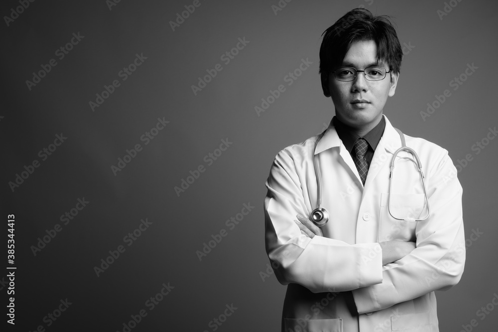 Young handsome Asian man doctor wearing eyeglasses against gray background Young handsome Asian man doctor wearing eyeglasses against gray background