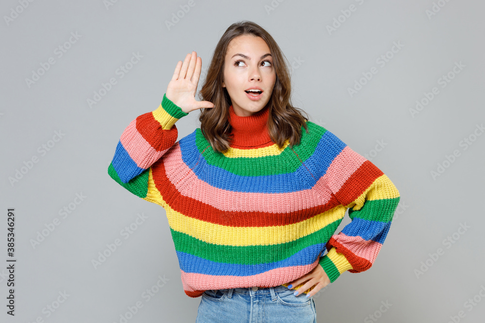 Shocked curious young brunette woman 20s wearing casual colorful knitted sweater standing try to hear you overhear listening intently looking aside isolated on grey colour background studio portrait. Shocked curious young brunette woman 20s wearing casual colorful knitted sweater standing try to hear you overhear listening intently looking aside isolated on grey colour background studio portrait.