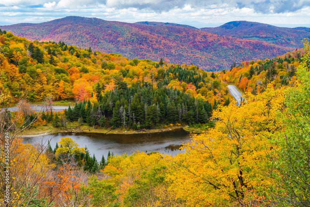 road winds through the Appalachian Gap, a mountain pass in the Green Mountains of Vermont, in bright colored fall foliage
