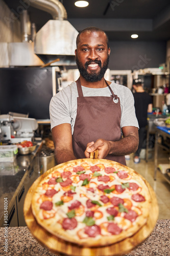 Cheerful young man holding wooden board with pepperoni pizza