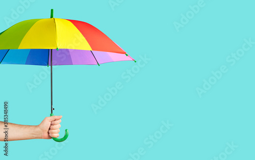 Rainbow-colored umbrella in male hand on green background