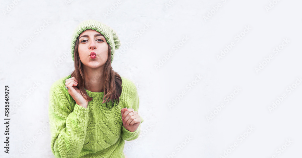 Woman in a knitted sweater and har sending an air kiss. Blank space for text on the background Woman in a knitted sweater and har sending an air kiss. Blank space for text on the background