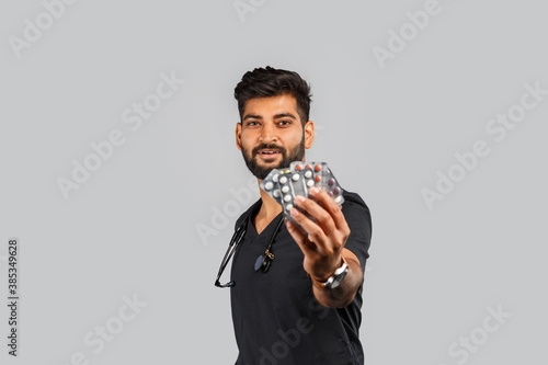 cute indian doctor or surgeon in black uniform with stethoscope and pills on gray background