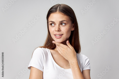 Happy woman touches her face with her hand and looks interested to the side 