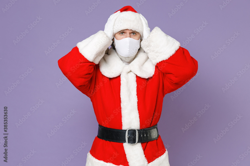 Worried Santa Claus man in Christmas hat suit mask to safe from coronavirus virus covid-19 during quarantine put hands on head isolated on violet background New Year celebration merry holiday concept. Worried Santa Claus man in Christmas hat suit mask to safe from coronavirus virus covid-19 during quarantine put hands on head isolated on violet background New Year celebration merry holiday concept.