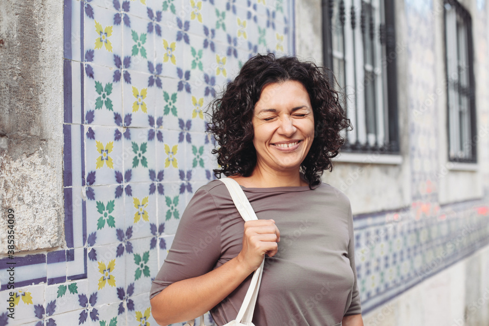 A happy woman with diastema, with curly hair laughing in Portugal. A wall with traditional Portuguese tiles - azulejo