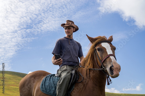 A rider in a wide-brimmed cowboy hat on a horse against a blue sky. © baxys