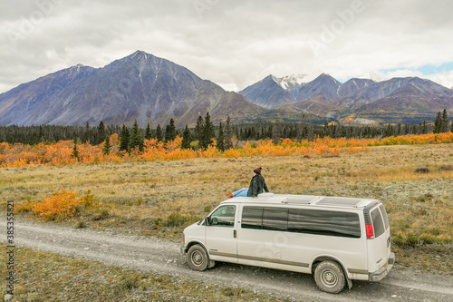 Woman sitting on top of a campervan camping with mountain view background, Epic, huge snow capped mountains in the distance, taken in the fall autumn season.  © Scalia Media