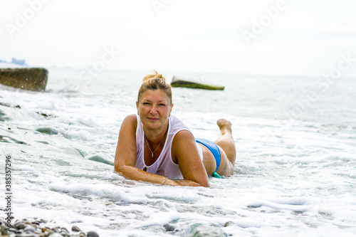 Young woman in a blue swimsuit sits on the seashore, waves and water cover the woman.