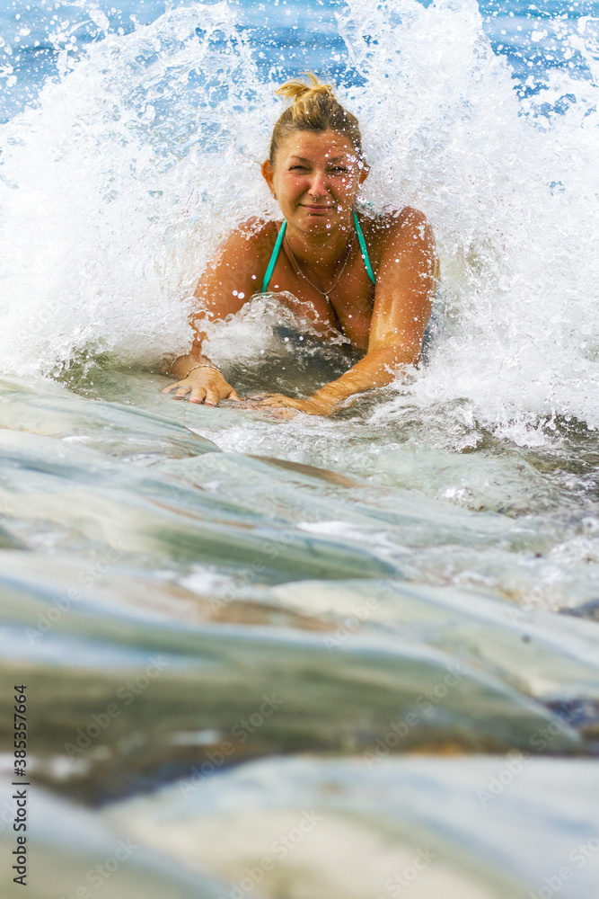 Obraz premium Young woman in a blue swimsuit sits on the seashore, waves and water cover the woman.