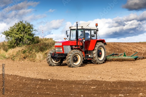 Red tractor cultivates the soil in the field with a cultivator after harvest. Autumn sunny day. Agricultural landscape in the Czech Republic. Work on the farm.