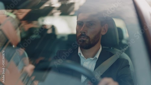 Portrait young confident man driving sitting in the car at sunset. Look around serious. Automobile work city. Driver businessman beard travel. Slow motion photo