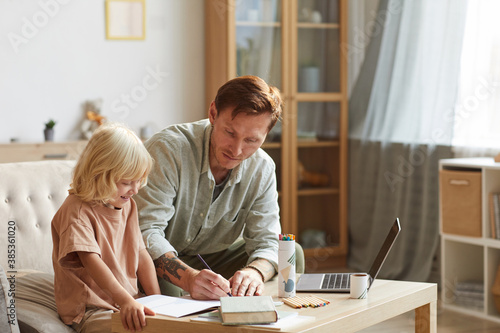 Father sitting at the table with his son and teaching him they are in the living room at home