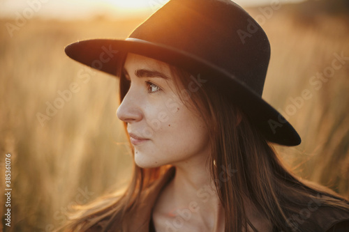 Portrait of calm boho woman in hat in sunset light on background of autumn field, carefree moment