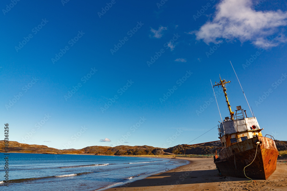 A wrecked ship on a sandy beach at low tide in the Teriberskaya Bay. Far North, Barents Sea in Russia.