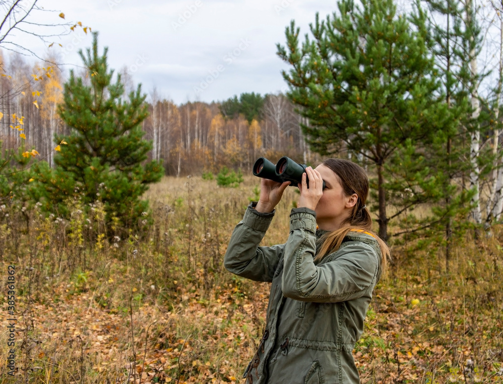 Young woman birdwatcher with binoculars in the autumn forest. Birdwatching, zoology, ecology. Research, observation of animals. Ornithology. Scientific research Young woman birdwatcher with binoculars in the autumn forest. Birdwatching, zoology, ecology. Research, observation of animals. Ornithology. Scientific research