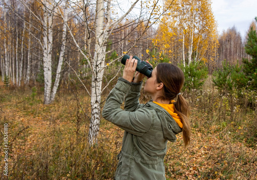 Young woman birdwatcher with binoculars in the autumn forest. Birdwatching, zoology, ecology. Research, observation of animals. Ornithology. Scientific research