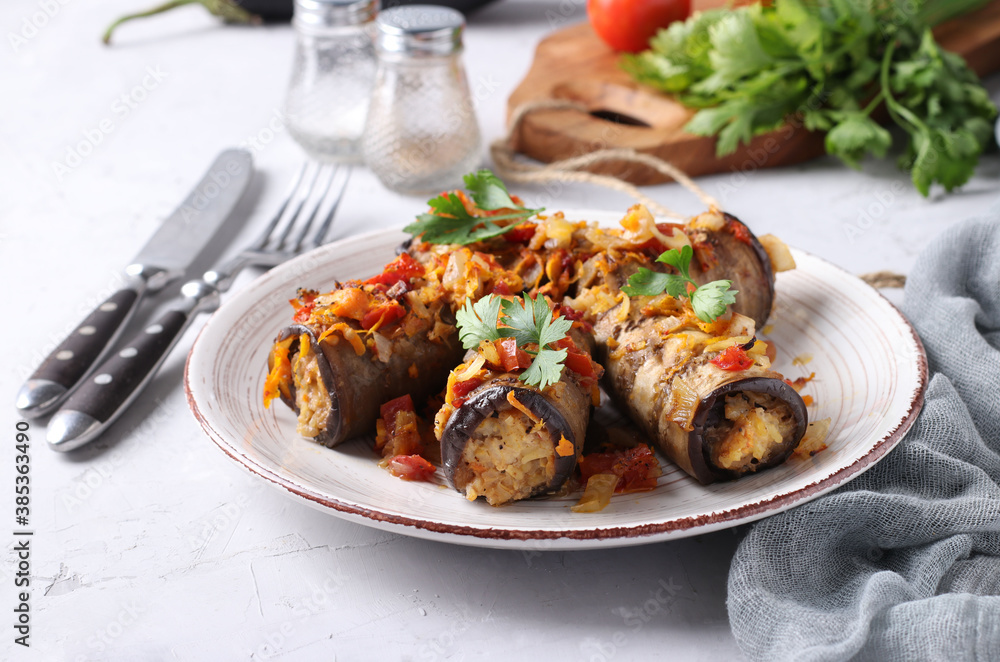 Baked eggplant rolls with chicken, onions and carrots in plate on gray background. Close-up. Baked eggplant rolls with chicken, onions and carrots in plate on gray background. Close-up.