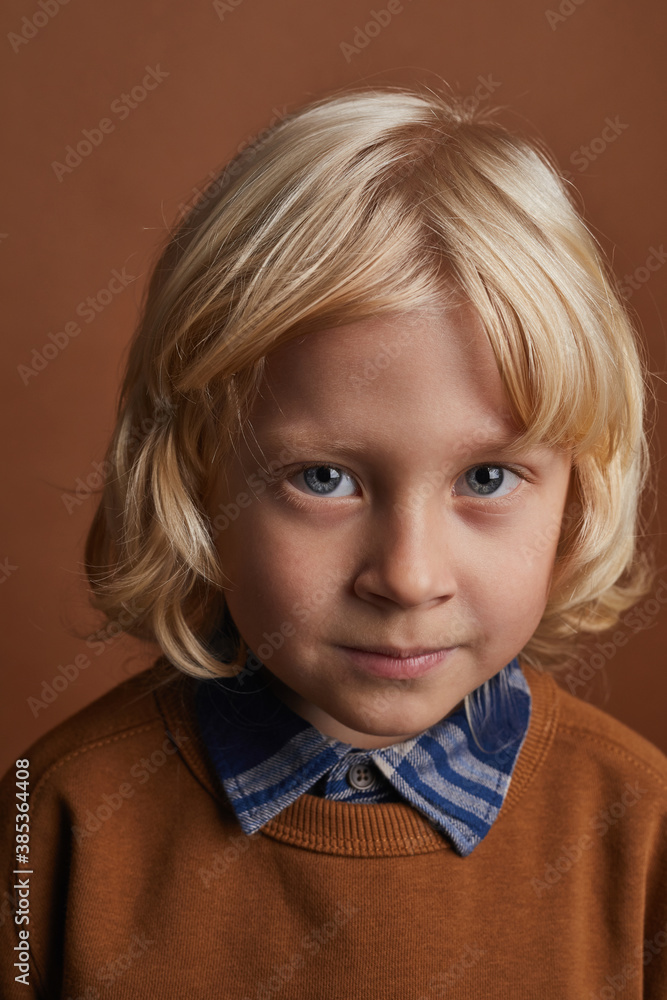 Portrait of little boy with long blonde hair looking at camera against the brown background Portrait of little boy with long blonde hair looking at camera against the brown background