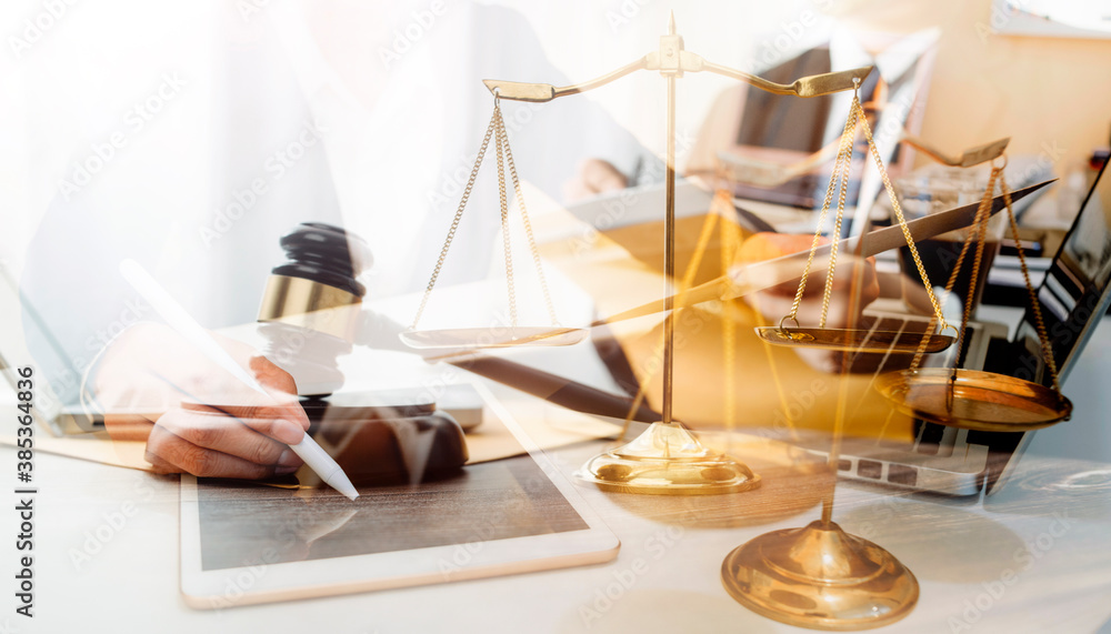 Justice and law concept.Male judge in a courtroom with the gavel, working with, computer and docking keyboard, eyeglasses, on table in morning light Justice and law concept.Male judge in a courtroom with the gavel, working with, computer and docking keyboard, eyeglasses, on table in morning light