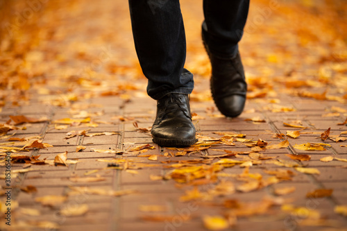 Men boots walking on the sidewalk strewn with autumn leaves