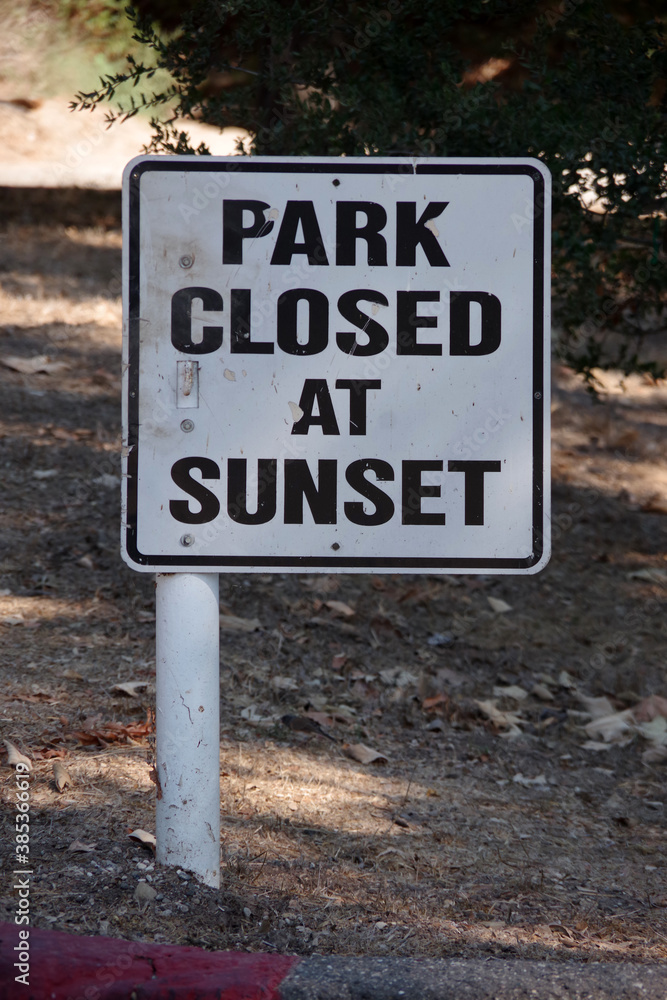 A posted sign at a public park entrance, PARK CLOSED AT SUNSET
