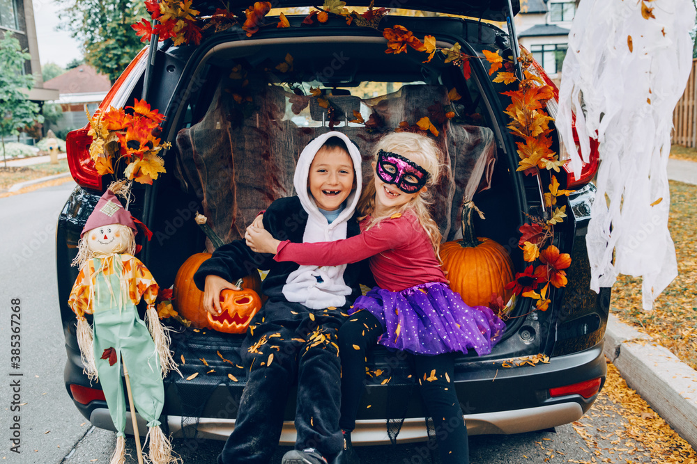 Trick or trunk. Children celebrating Halloween in trunk of car. Boy and girl with red pumpkins celebrating traditional October holiday outdoors. Social distance and safe alternative celebration. - obrazy, fototapety, plakaty 