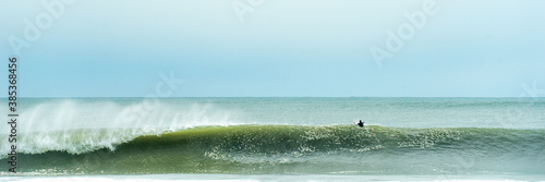 A lone surfer paddles over a large breaking wave. Long Beach Surfing New York