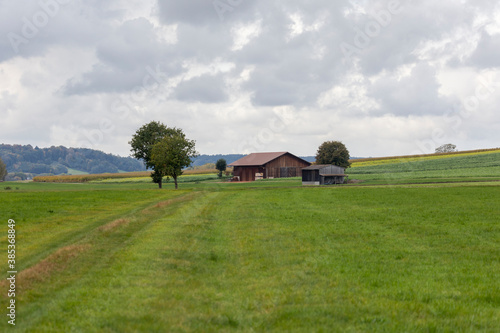 A dirt road leads to a barn between meadows in cloudy weather