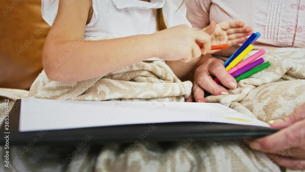 Unknown granny and her little grandchild are drawing with felt-tip pens on a sheet of paper, sitting on sofa at home Unknown granny and her little grandchild are drawing with felt-tip pens on a sheet of paper, sitting on sofa at home