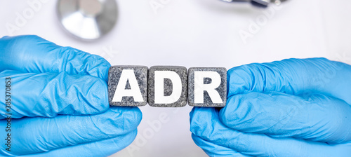 ADR Adverse drug reaction - word from stone blocks with letters holding by a doctor's hands in medical protective gloves