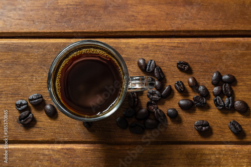 Xícara com café e grãos de café espalhados sobre superfície de madeira.