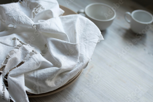 a stack of plates with an embroidered crumpled napkin, two eggs and two empty tea cups on a gray wooden kitchen table