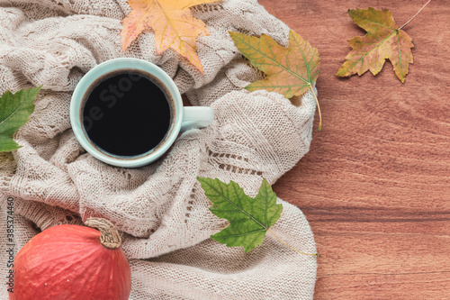 A cup of coffee on the table with pumpkin, autumn leaves and a knitted sweater. Autumn concept, top view