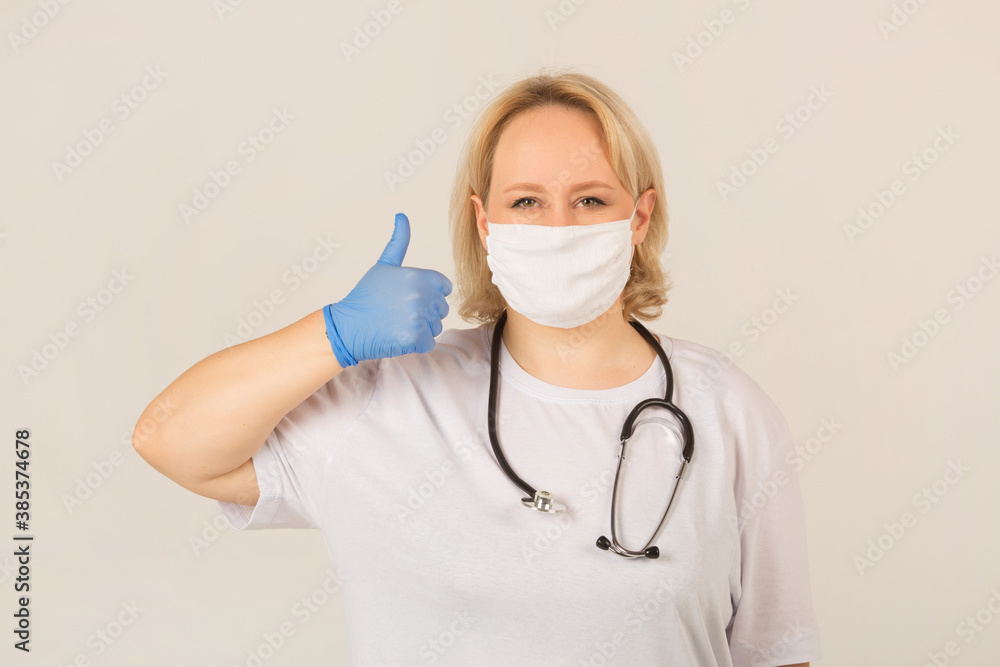 beautiful young plump female in white t-shirt with stethoscope in protective mask with hand gesture beautiful young plump female in white t-shirt with stethoscope in protective mask with hand gesture