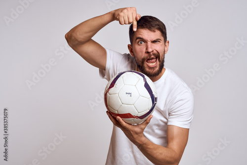 Male coach with a soccer ball in his hands on a light background energy explanation of movements © SHOTPRIME STUDIO